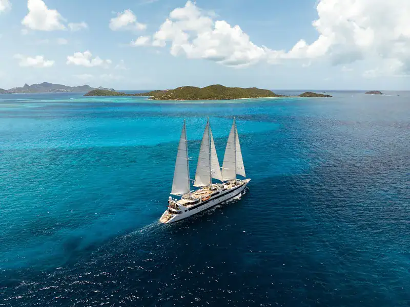 Barco de vela navegando en aguas turquesas cerca de islas tropicales.
