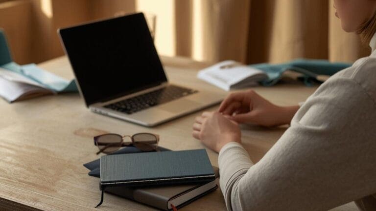 Personas trabajando en un escritorio con laptop y libros en un ambiente de oficina.