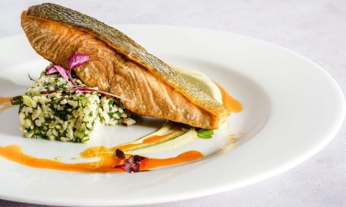 Pez de salmón a la plancha con ensalada y salsa en plato blanco.