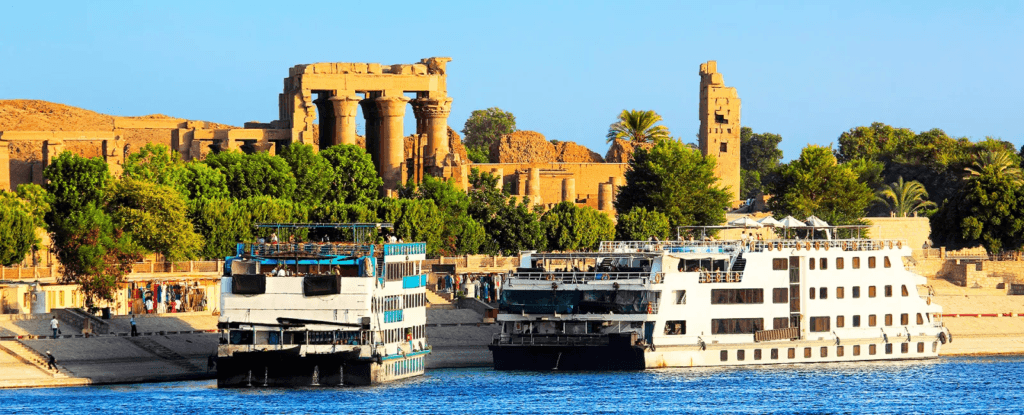 Barcos turísticos navegando por el río Nilo con ruinas antiguas al fondo.
