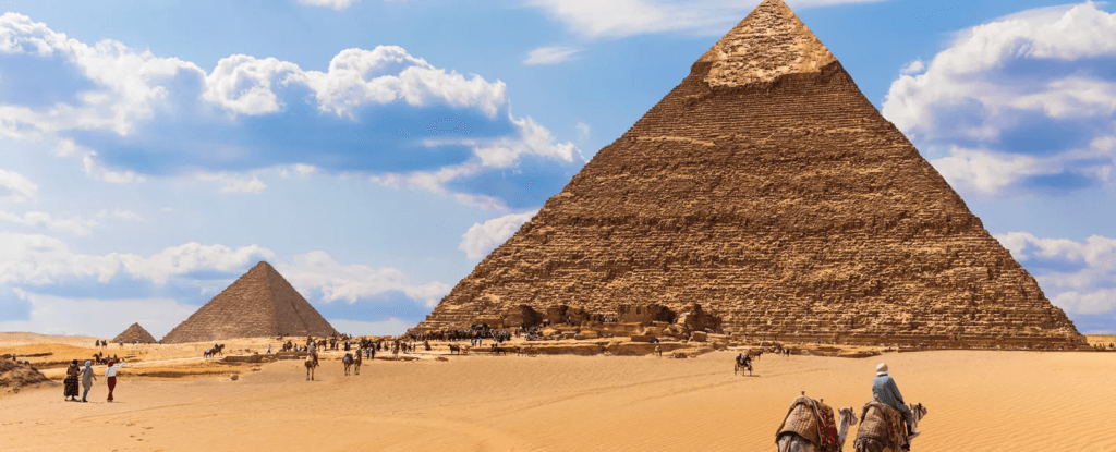 Pirámides de Egipto en el desierto, con turistas y camellos en primer plano.