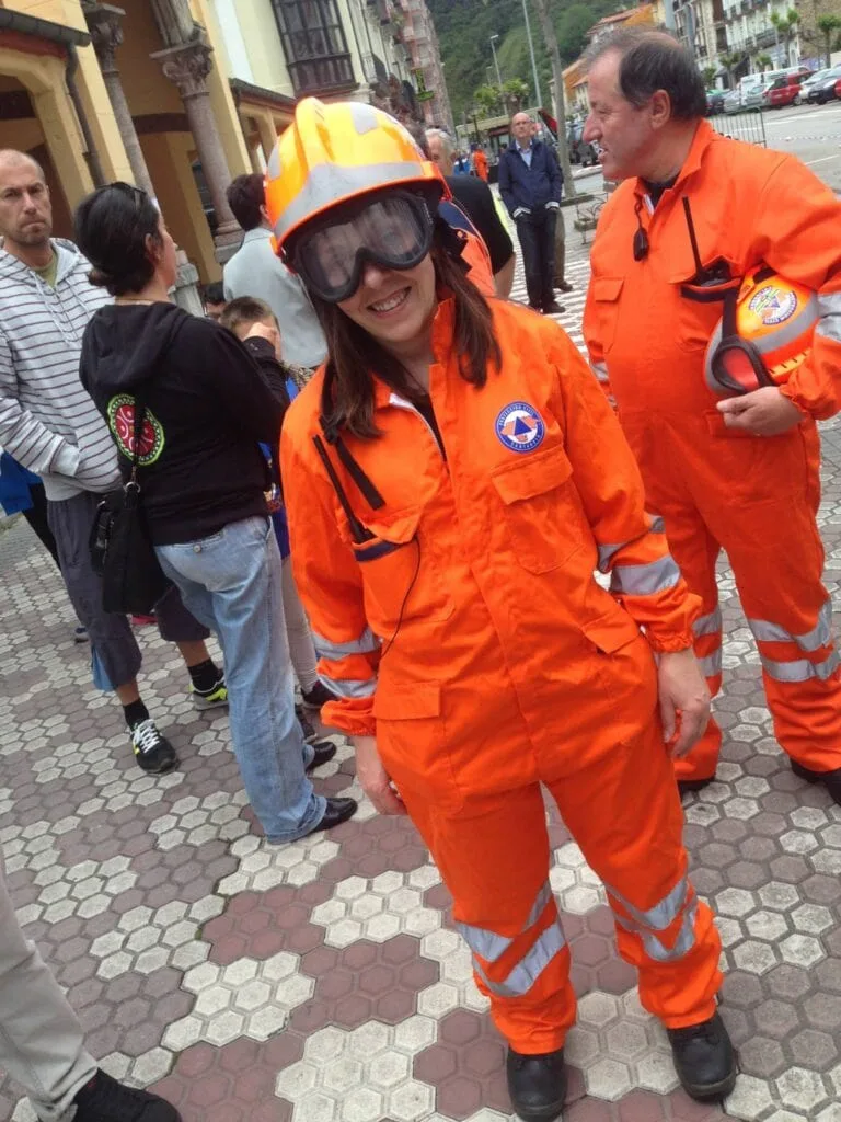 Personal de emergencia en uniforme naranjas en una calle concurrida, sonriendo y interactuando con personas.
