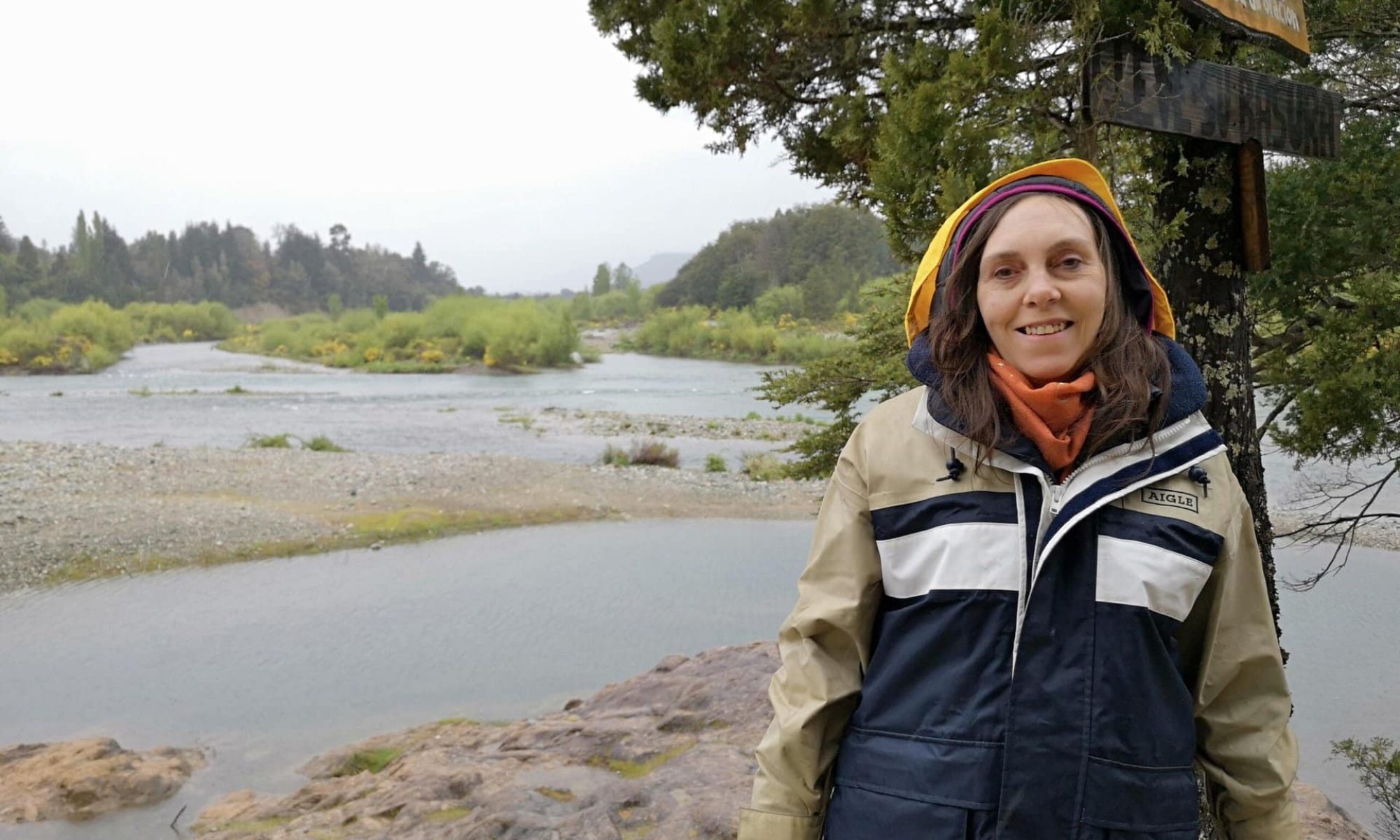 Mujer disfrutando de la naturaleza junto a un río en un día lluvioso.